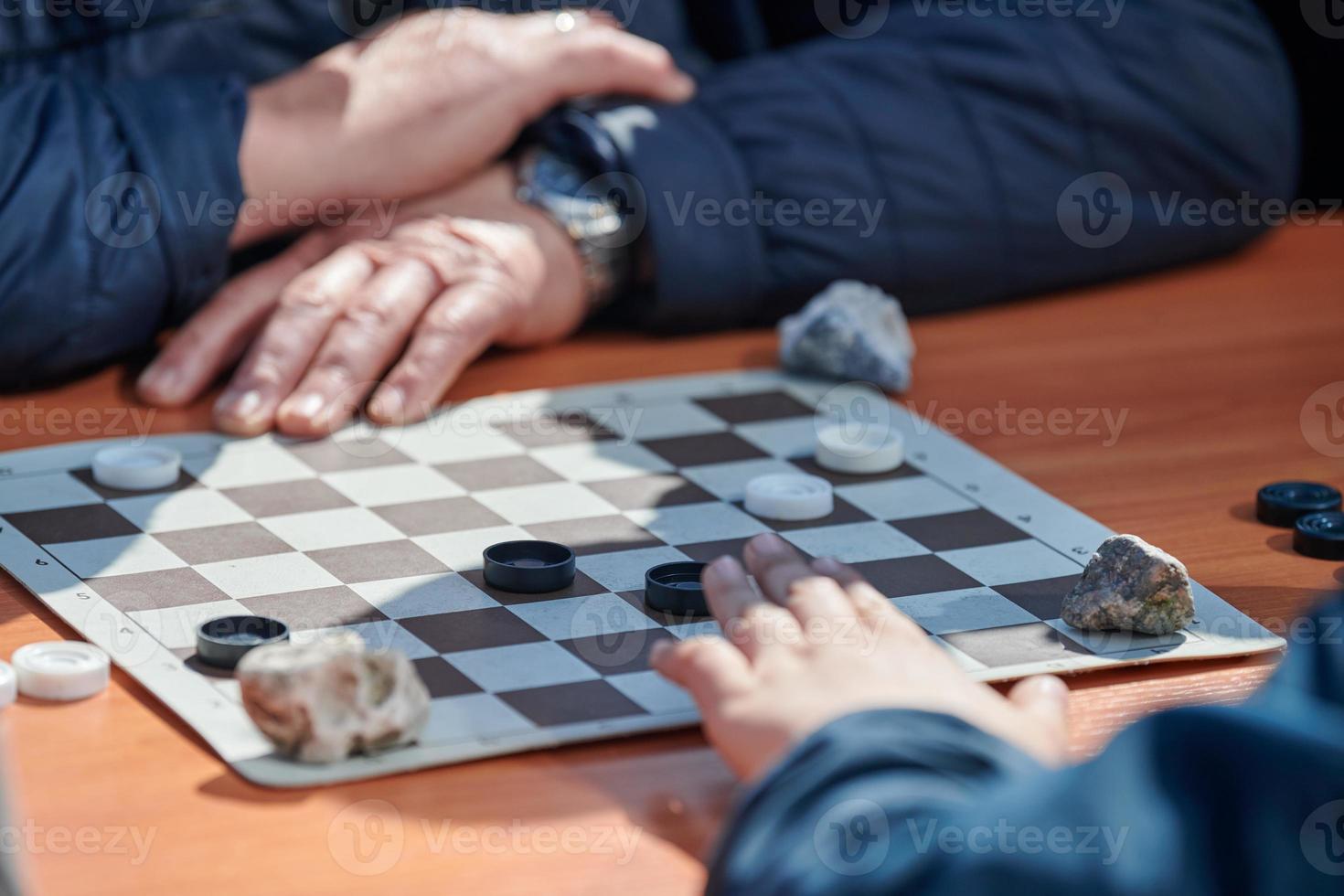 Outdoor checkers tournament on paper checkerboard on table, close up players hands photo