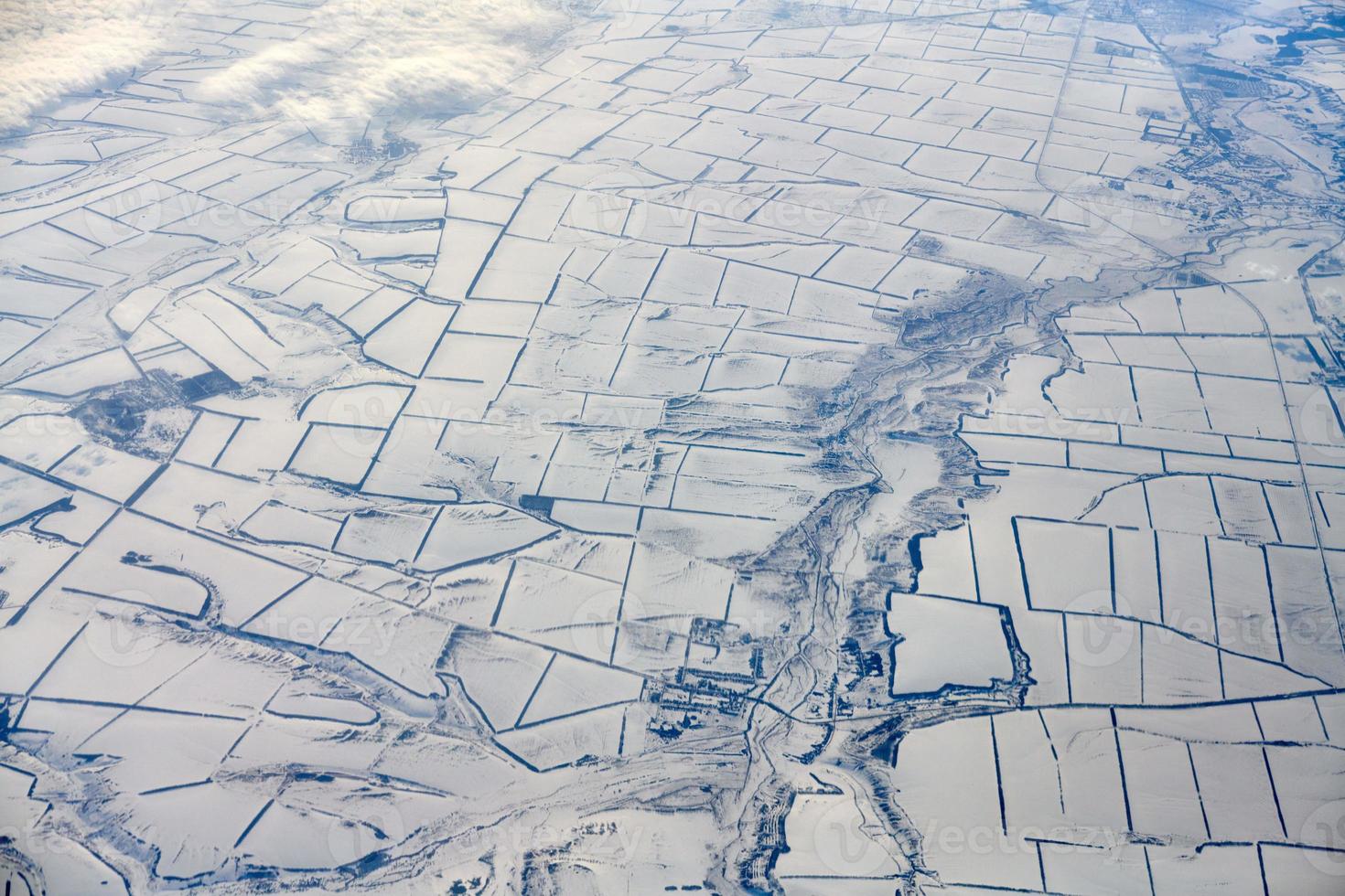 Aerial cloudscape view over clouds top to snow covered rivers, roads, cities and fields, winter air photo