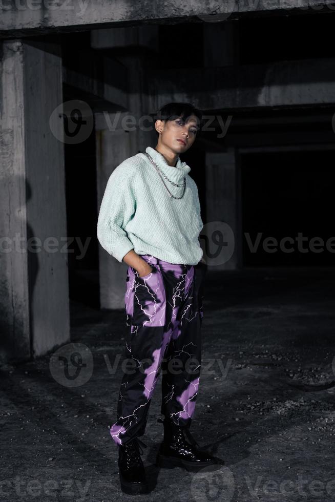 an asian man in black pants with a lightning pattern and a white sweater stands photo