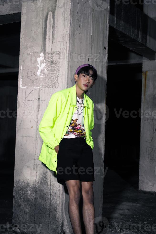 an asian man in a lime colored jacket leaning against a disused building pillar looking very handsome photo