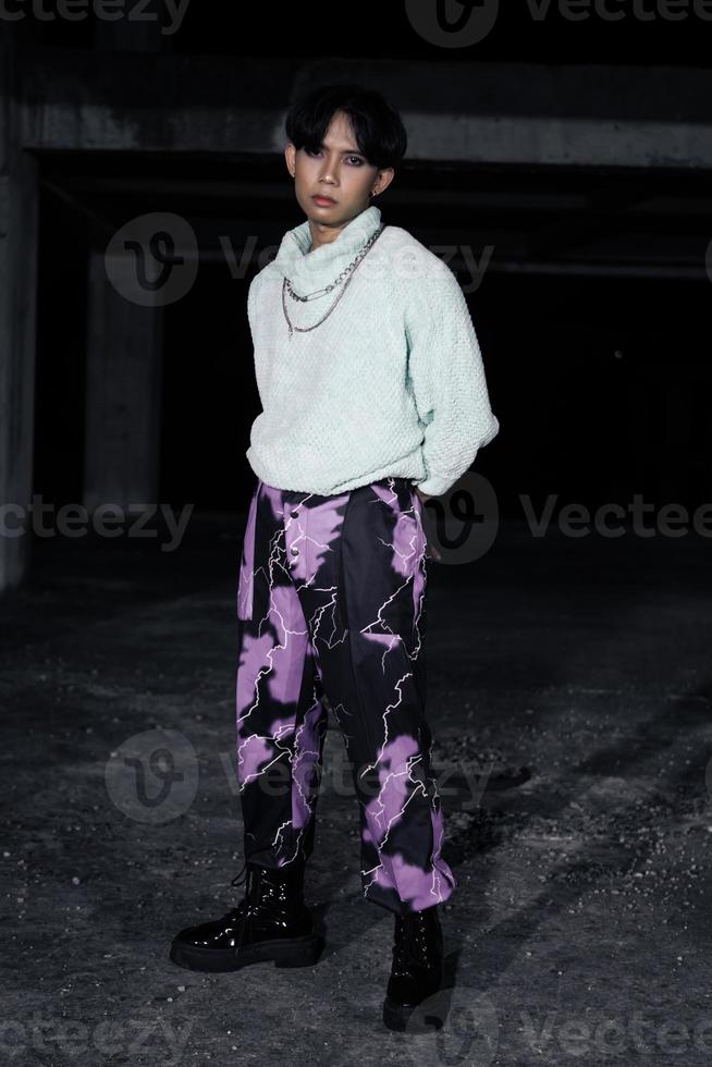 an asian man in black pants with a lightning pattern and a white sweater stands photo