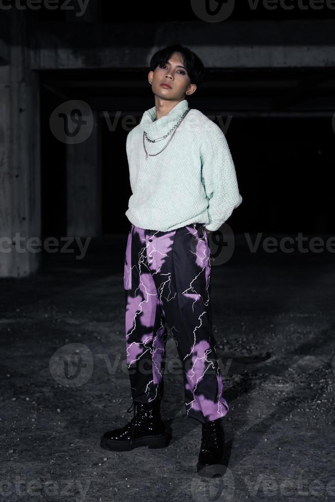 an asian man in black pants with a lightning pattern and a white sweater stands photo