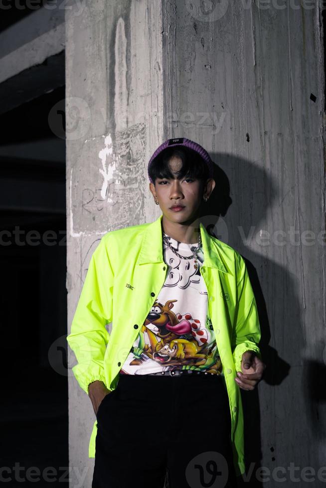 an asian man in a lime colored jacket leaning against a disused building pillar looking very handsome photo