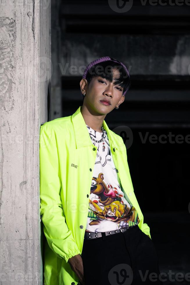 an asian man in a lime colored jacket leaning against a disused building pillar looking very handsome photo