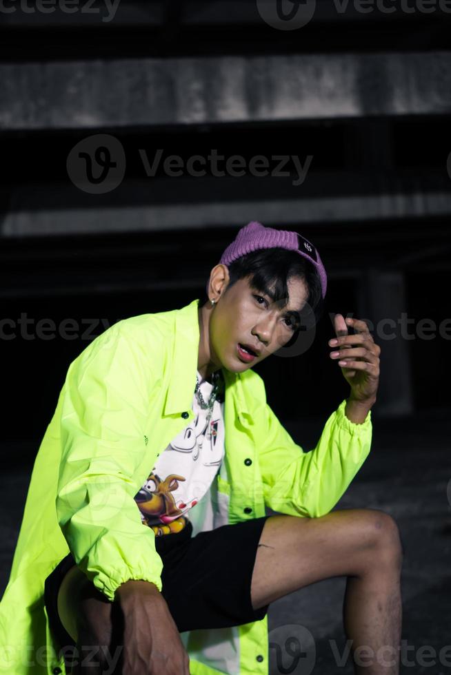 an asian man in a green jacket posing and sitting very casually photo