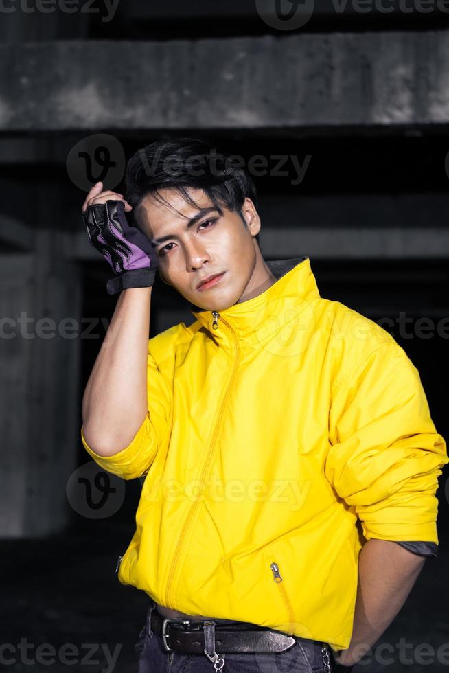 an Asian man with sleek black hair wearing a yellow jacket and jeans while posing photo