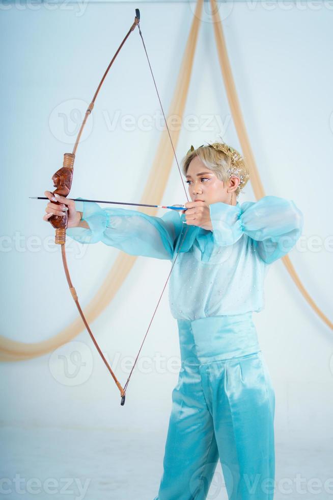 un asiático mujer con rubia pelo participación un flecha mientras vistiendo un azul vestir foto