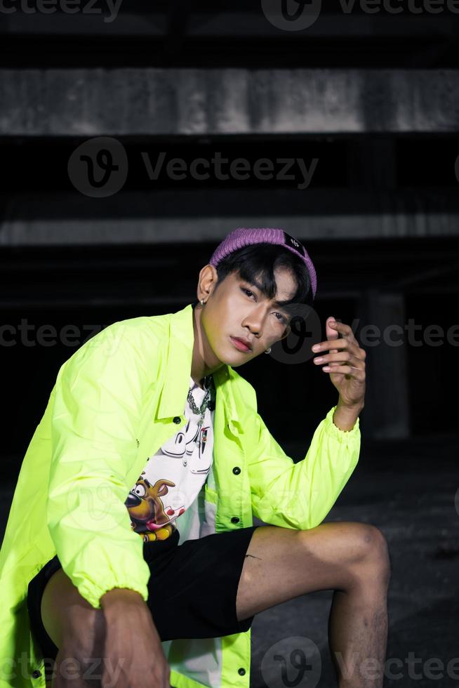 an asian man in a green jacket posing and sitting very casually photo