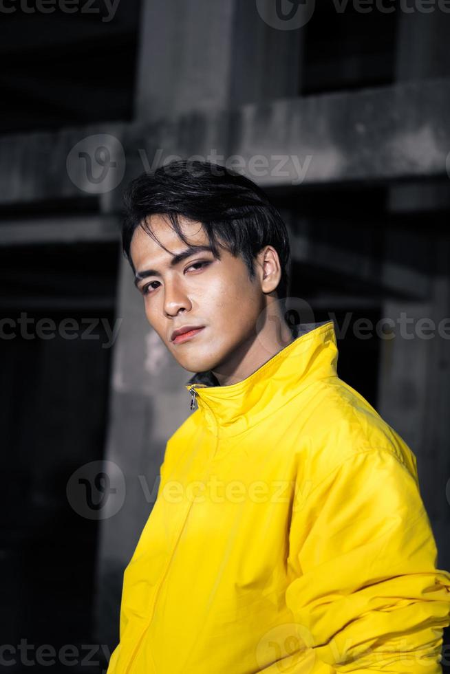 an Asian man with sleek black hair wearing a yellow jacket and jeans while posing photo