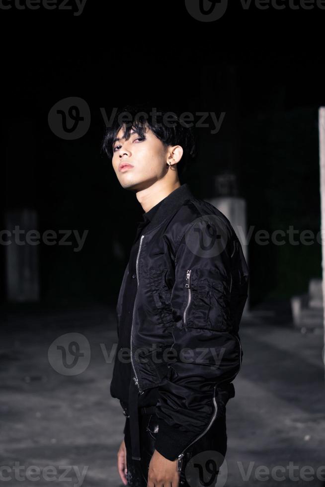 an asian man in a black parachute jacket posing very manly in a building photo