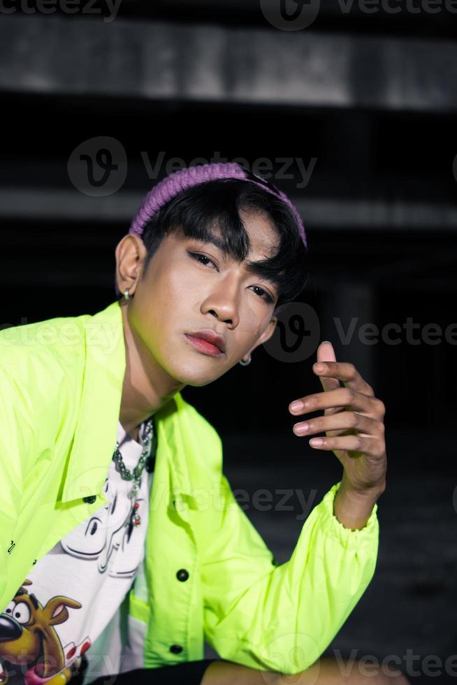 an asian man in a green jacket posing and sitting very casually photo