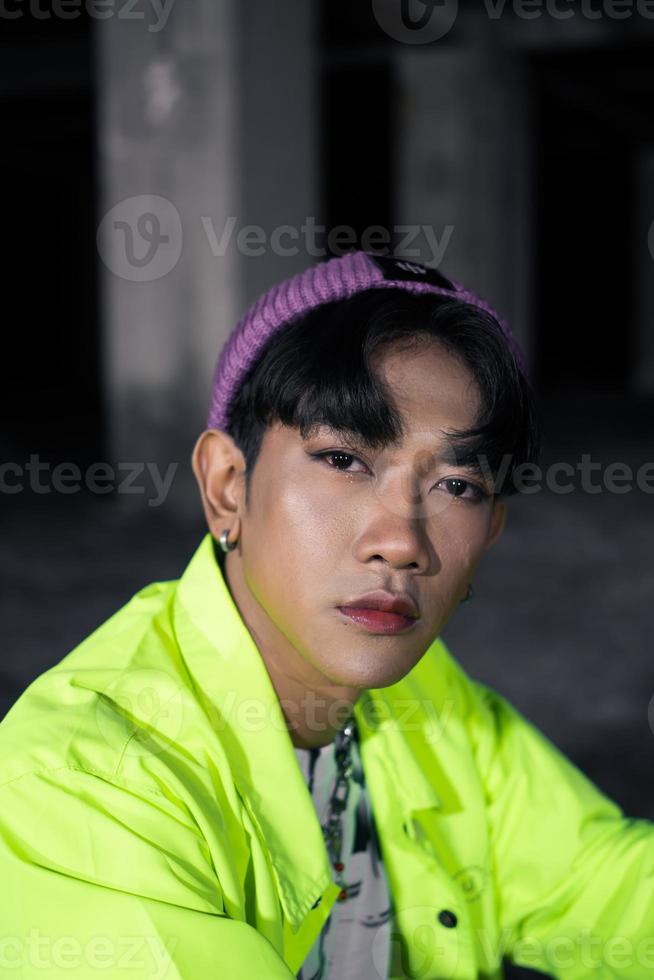 an asian man in a green jacket posing and sitting very casually photo