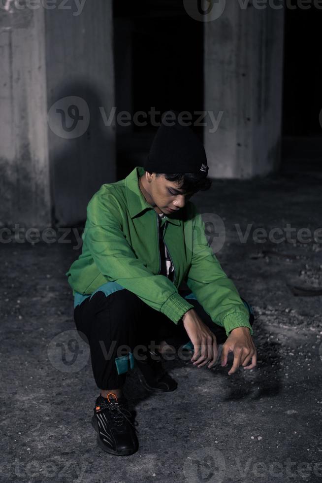 an Asian man squats while wearing a green jacket photo