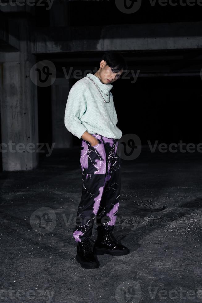 an asian man in black pants with a lightning pattern and a white sweater stands photo
