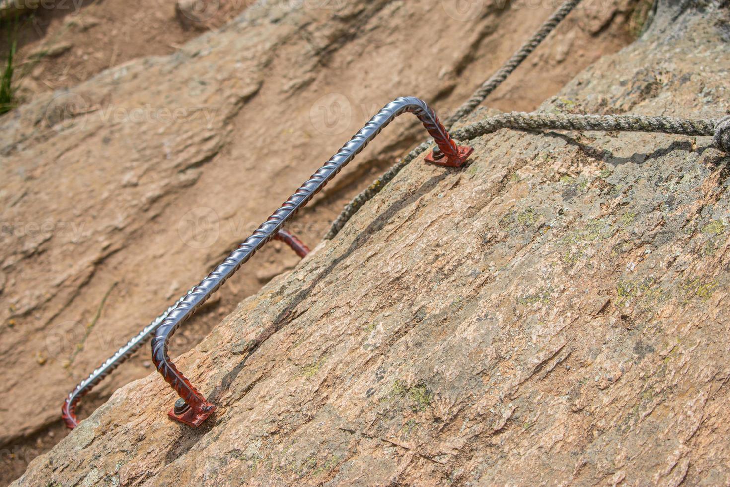 metal rung on rock wall with rope to climb up photo