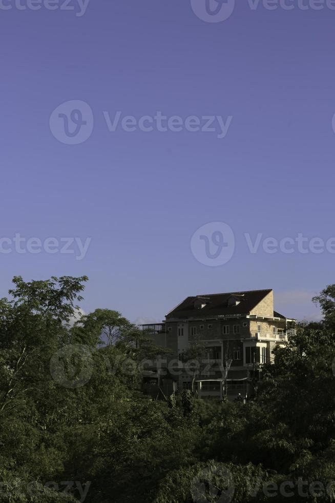 A calming residential district with tall buildings, lush trees and plants, atop a hill framed by bright blue sky. photo