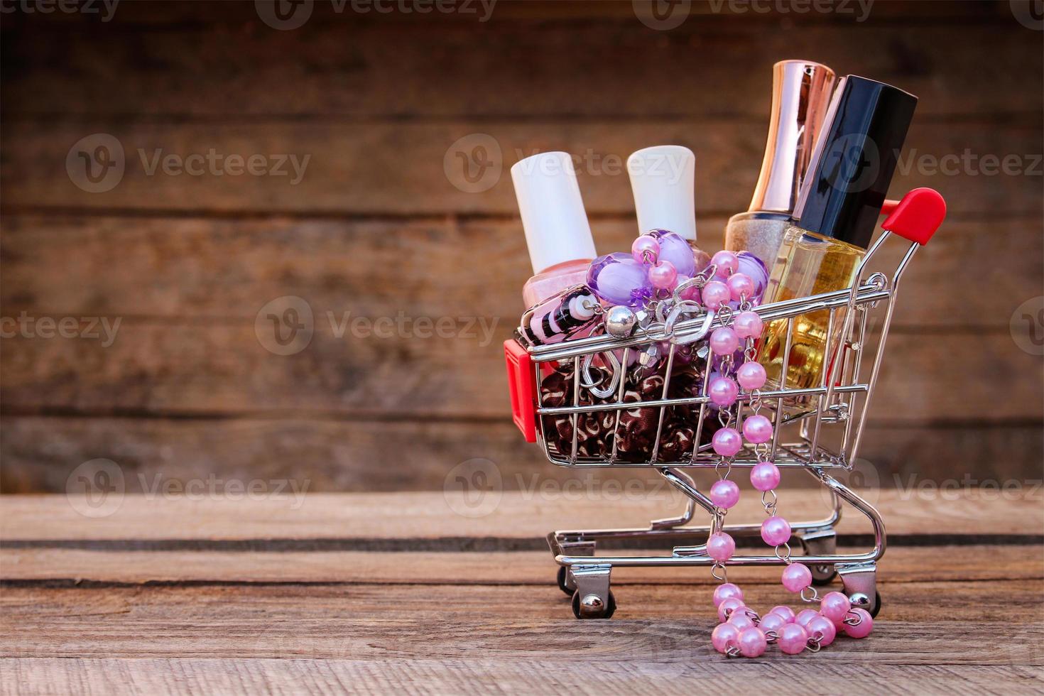 Shopping cart with cosmetics, bead, hair clip on the old wood background. Toned image. photo
