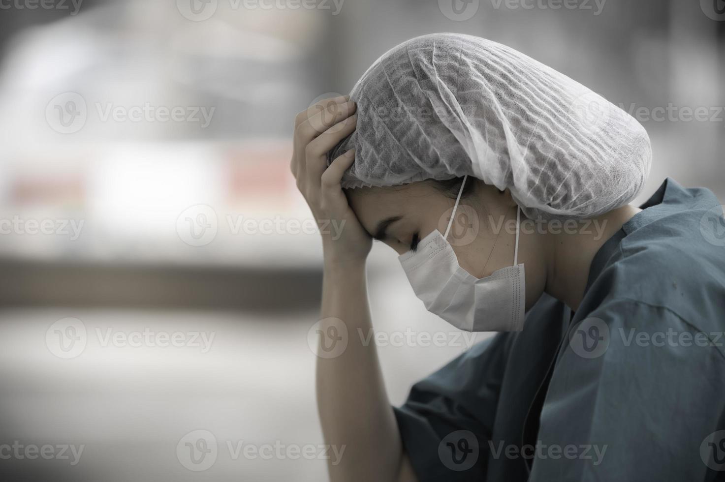 Tired depressed female asian scrub nurse wears face mask blue uniform sits on hospital floor,Young woman doctor stressed from hard work photo