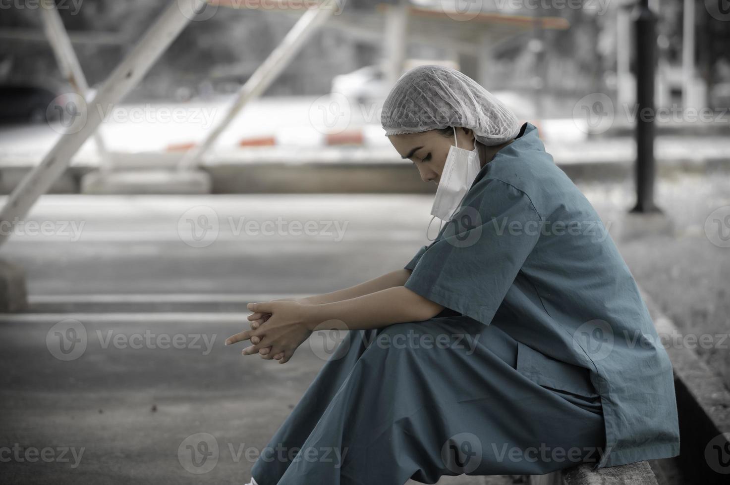 Tired depressed female asian scrub nurse wears face mask blue uniform sits on hospital floor,Young woman doctor stressed from hard work photo