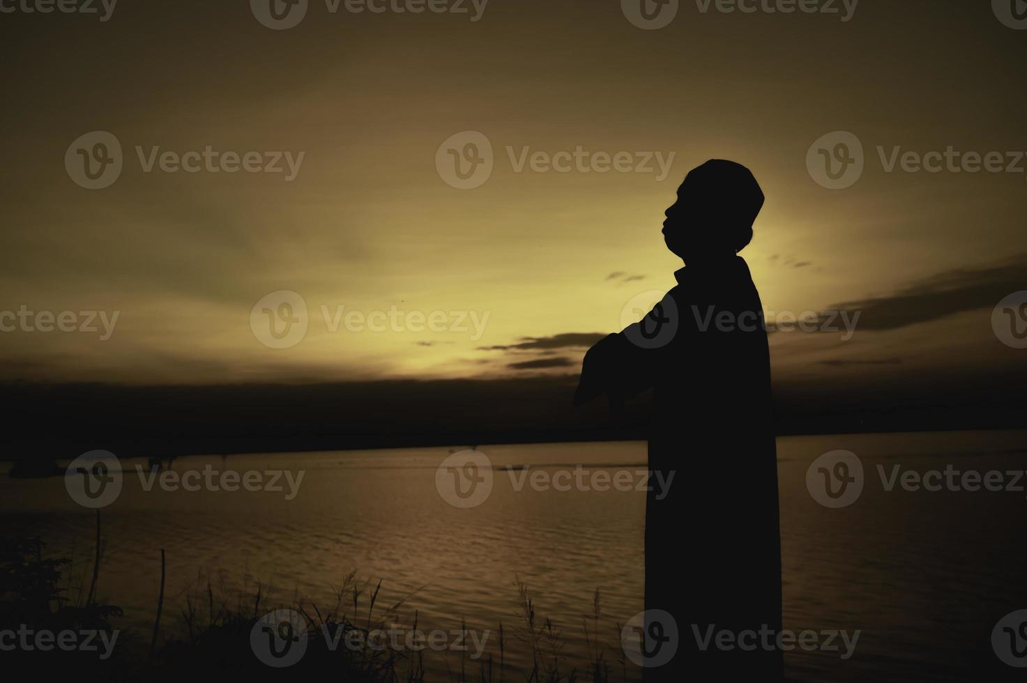 silueta joven asiático musulmán hombre Orando en puesta de sol, ramadán festival concepto foto