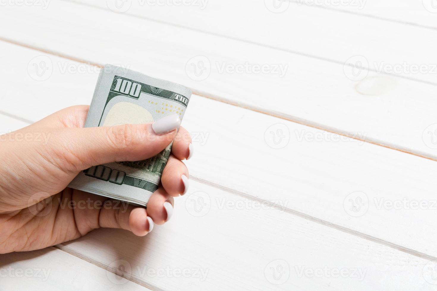 Perspective view of female hand holding a pack of money on wooden background. One hundred dollars. Business concept with empty space for your design. Charity and tips concept photo