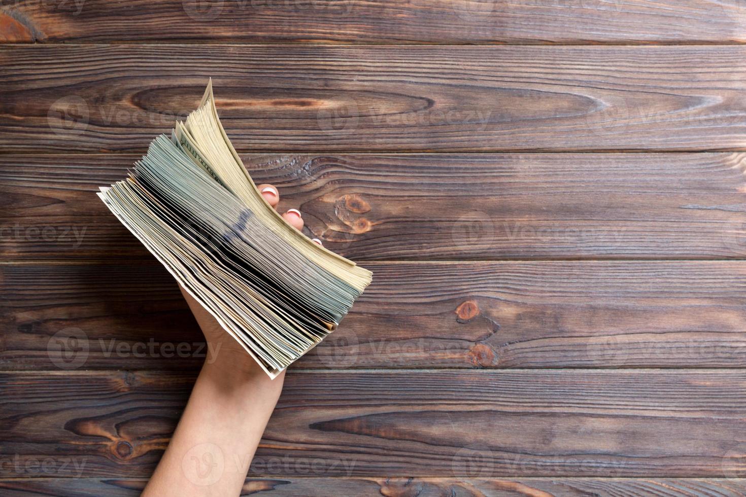 Female hand holding a big and thick bundle of various dollar banknotes on wooden background. Salary and wage concept with copy space photo