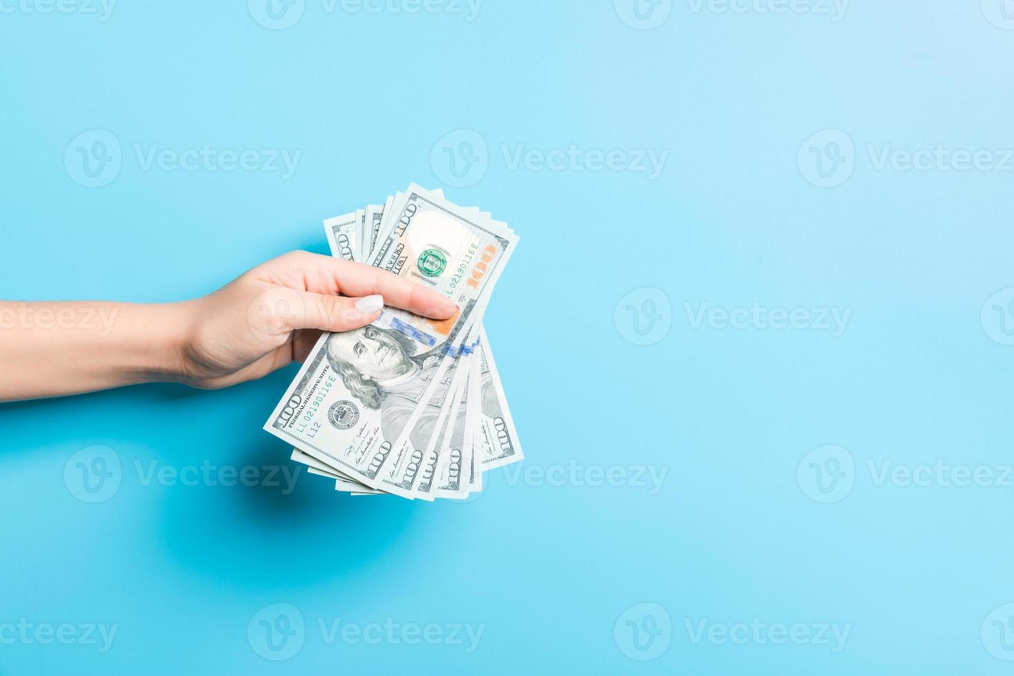 Female hand giving money on blue background. Dollar banknotes. Bribe concept. Debt and loan concept photo