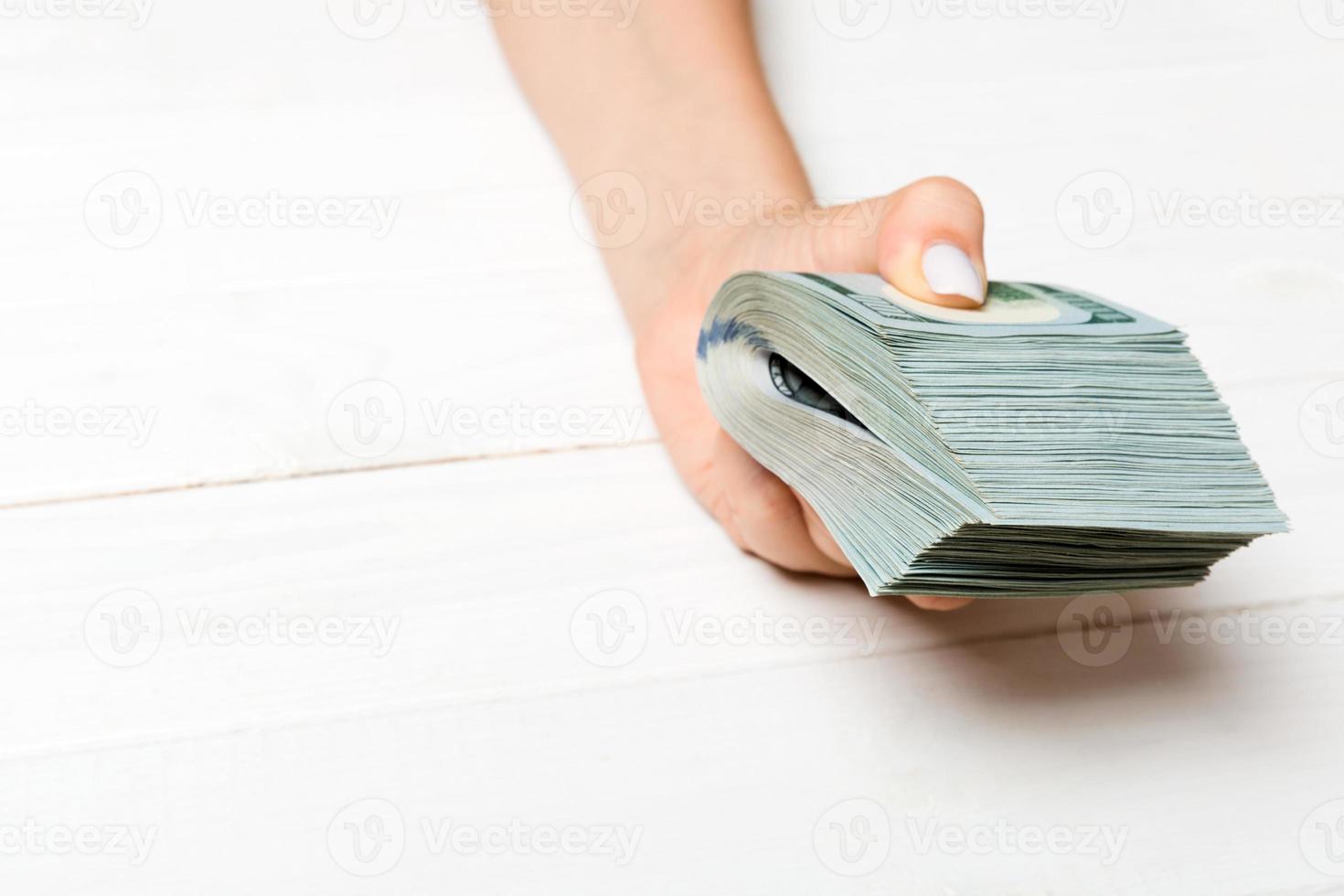 Perspective view of female hand holding a pack of money on wooden background. One hundred dollars. Business concept. Charity and tips concept photo