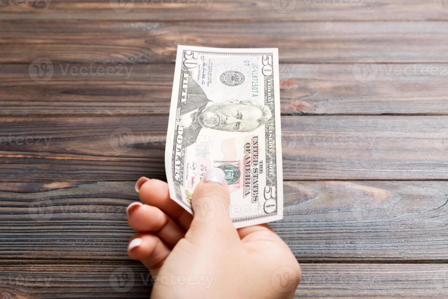 Female hand holding fifty dollar banknote on wooden background. Salary and wage concept photo