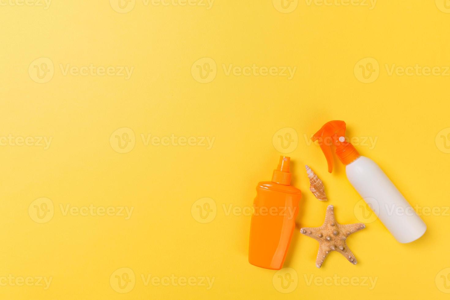 sunscreen cream with starfish and seashells in bottles on yellow background, top view photo