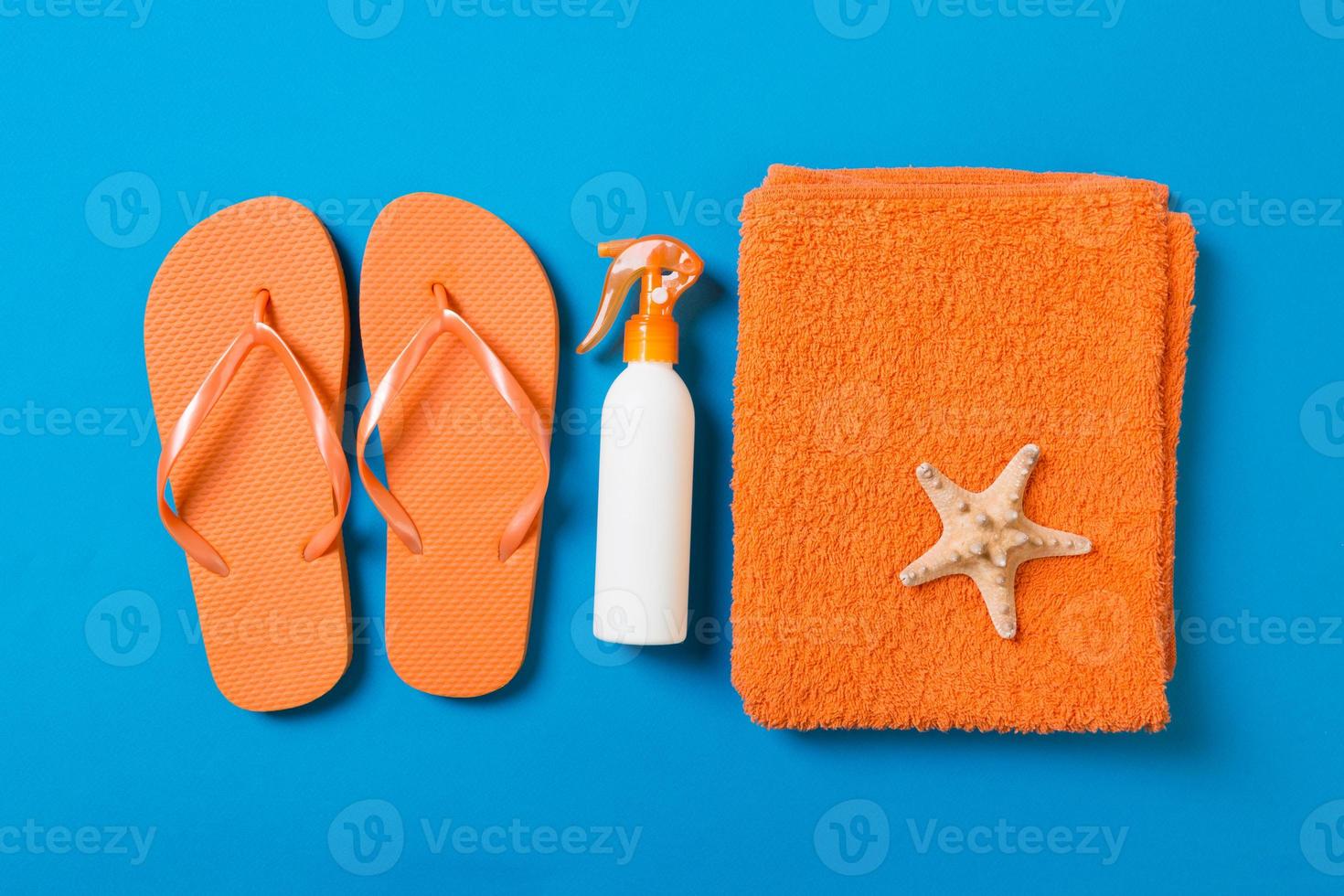 Top view of Beach flat lay accessories. sunscreen bottle with seashells, starfish, towel and flip-flop on Colored background with copy space photo