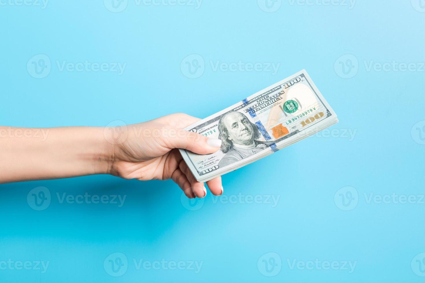 Female hand giving a bundle of dollar bills on blue background. Power and wealth concept photo