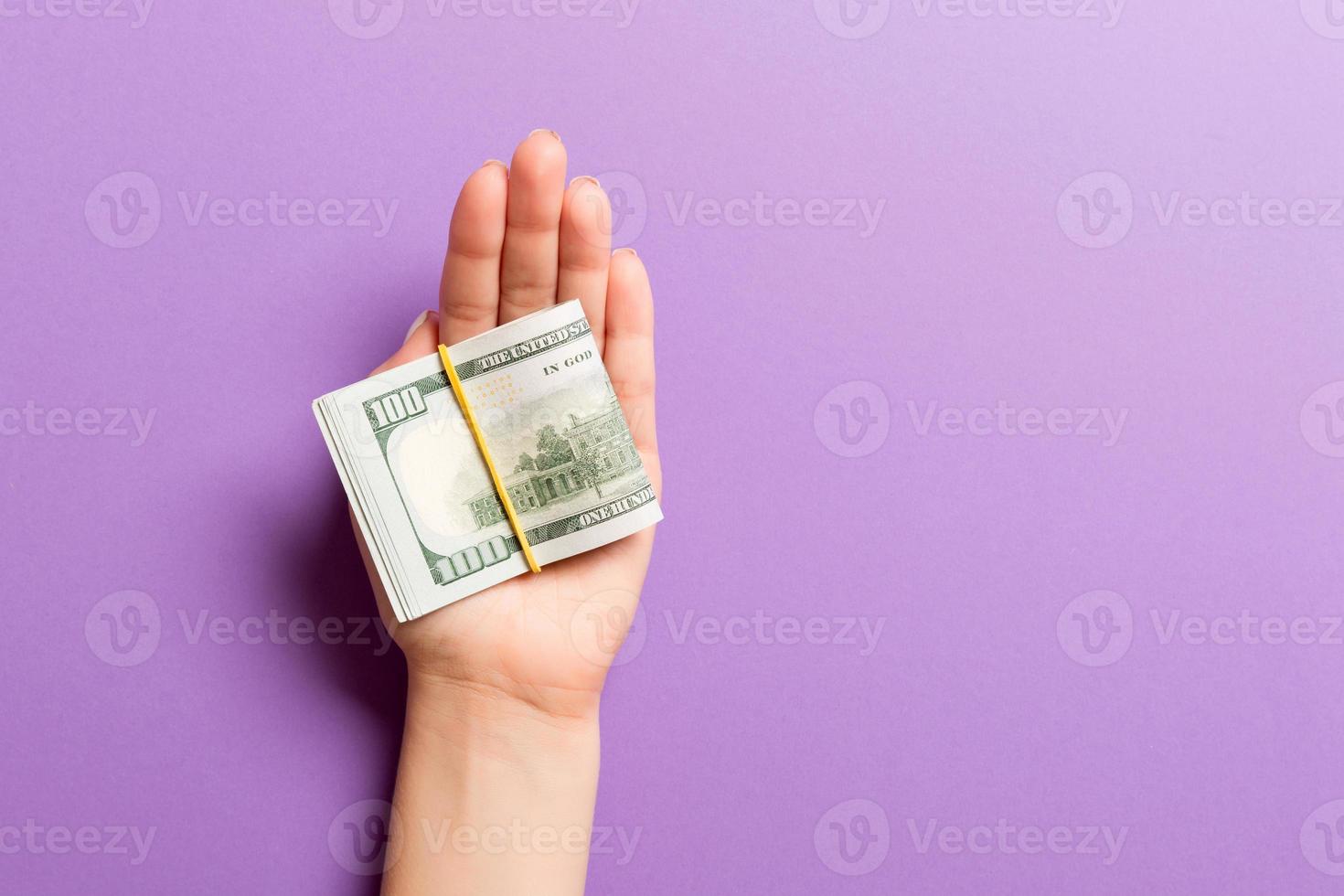 Top view of female hand holding a lot of rolled up dollar banknotes on colorful background. Poverty concept. Credit concept with copy space photo