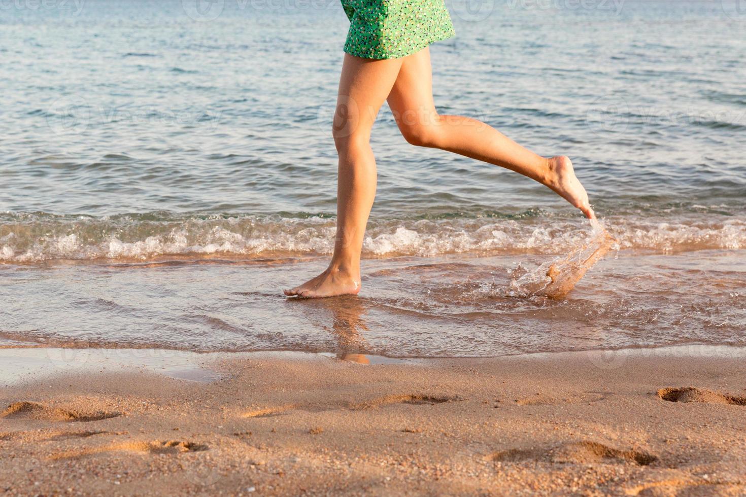 Leg of woman running on beach with water splashing. summer vacation. legs of a girl walking in water on sunset photo