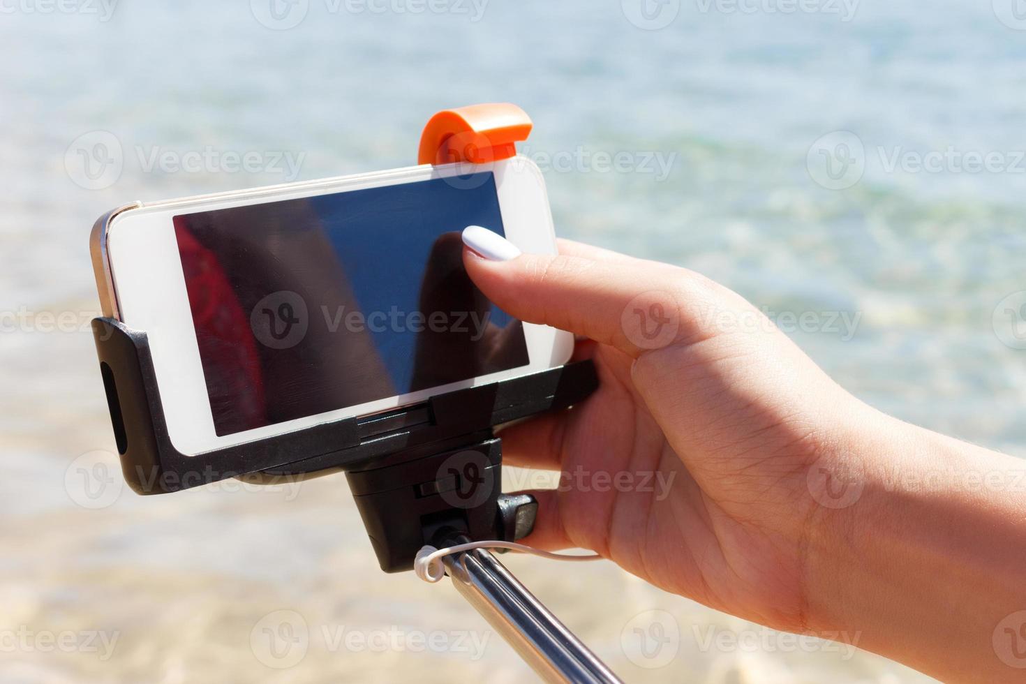 girl adjusts camera on selfie stick in the sea photo