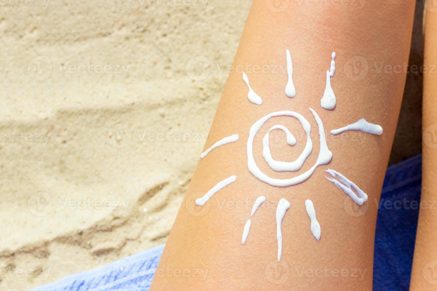 Woman sunbathing on the beach with a drawing of sun on her leg with sunscreen cream photo