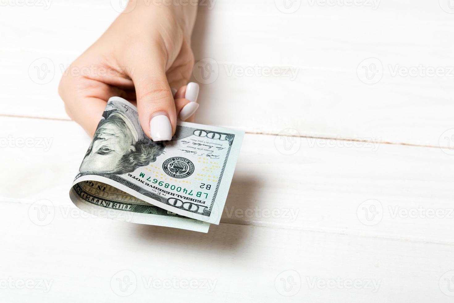 A pack of one hundred dollar bills in female hand on wooden background. Salary concept with copy space photo