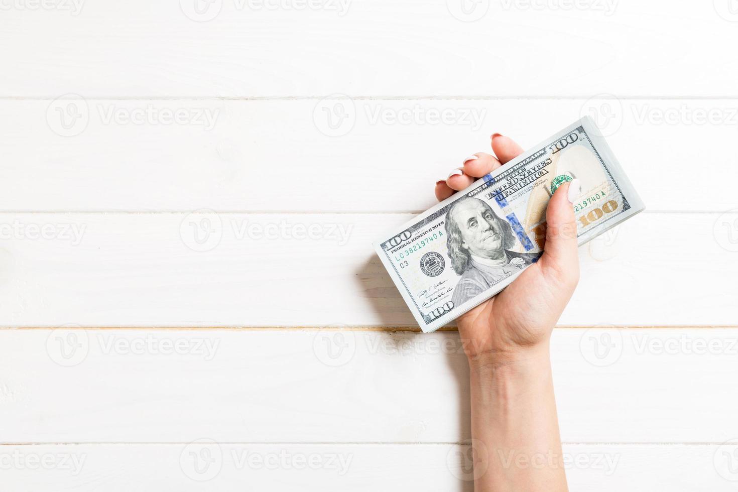 Female hand holding a bundle of money on colorful background. Top view of one hundred dollar banknotes. Salary concept with empty space for your design photo
