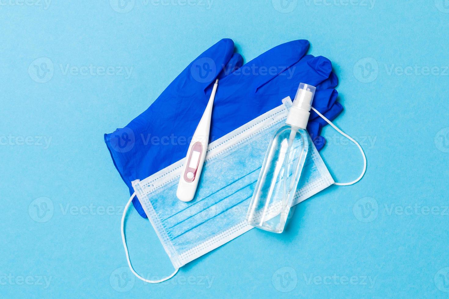 Top view of latex gloves, bottle of alcohol hand sanitizes, medical mask and digital thermometer on blue background. Antibacterial virus protection concept with copy space photo