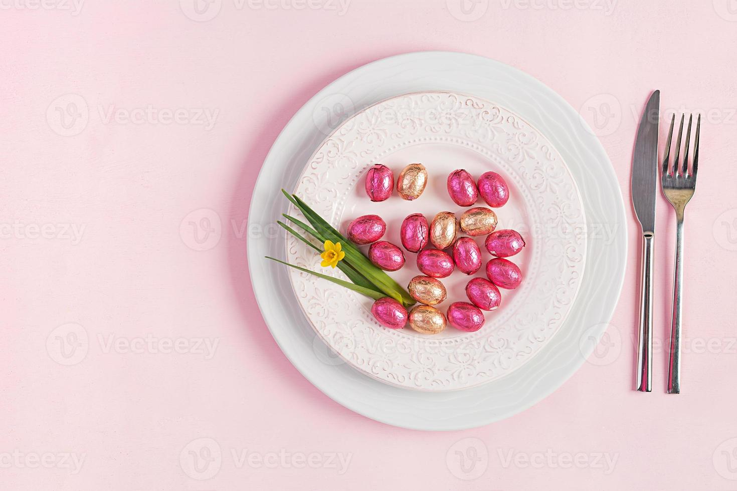 contento Pascua de Resurrección. mesa ajuste para Pascua de Resurrección día festivo. Pascua de Resurrección huevos, flor y cuchillería en rosado antecedentes. parte superior vista, plano laico foto