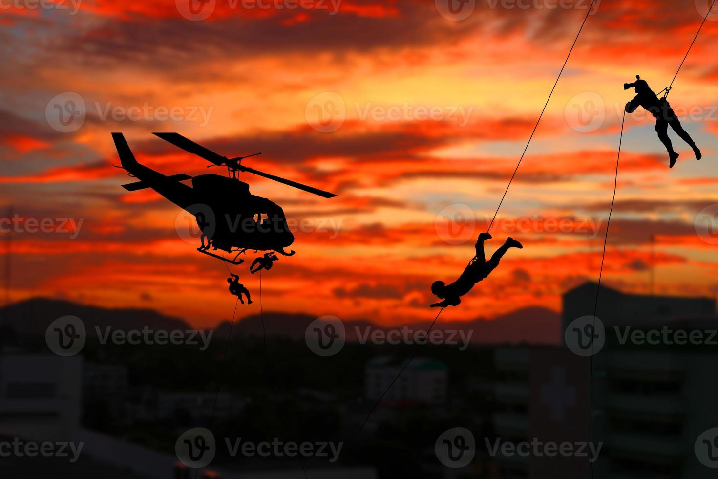 Silhouette Soldiers rappel down to attack from helicopter with sunset and copy space add text photo