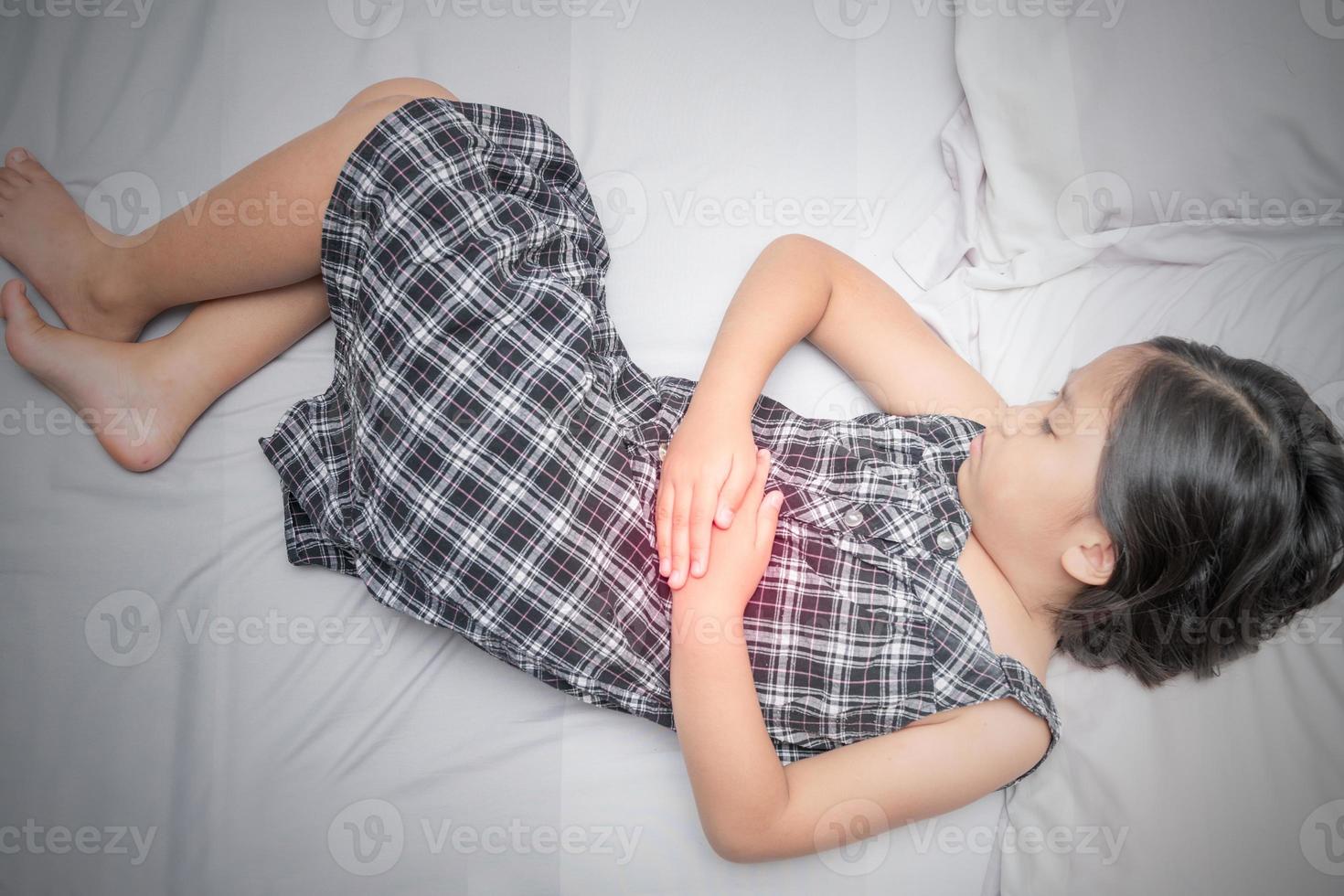 Asian girl suffering from stomachache on bed photo