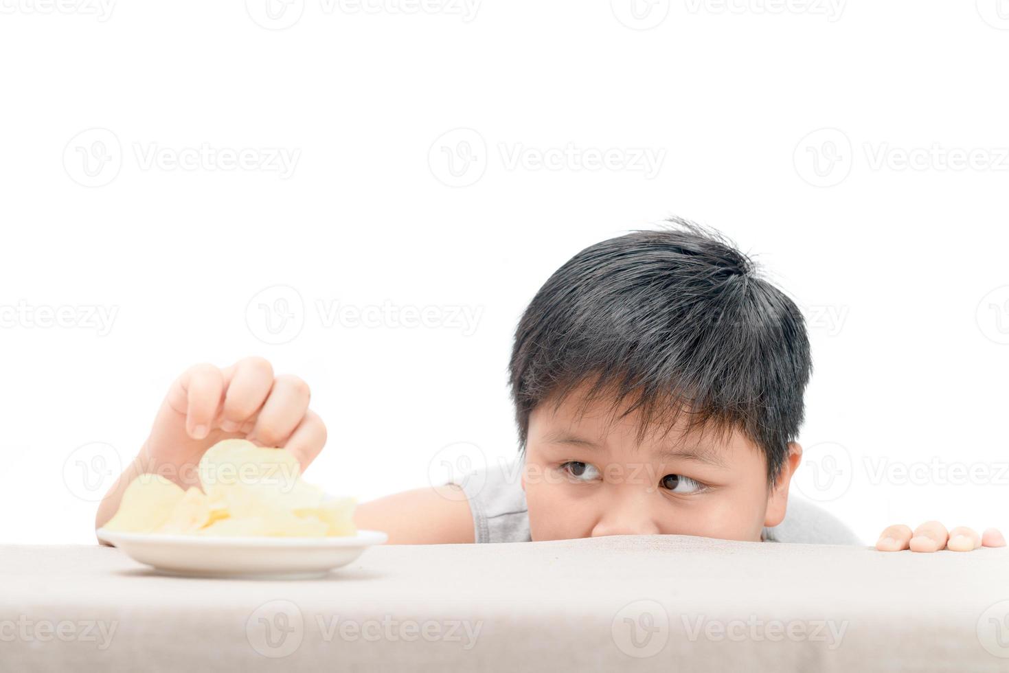 Obese fat boy is reaching  potato crisps on table photo
