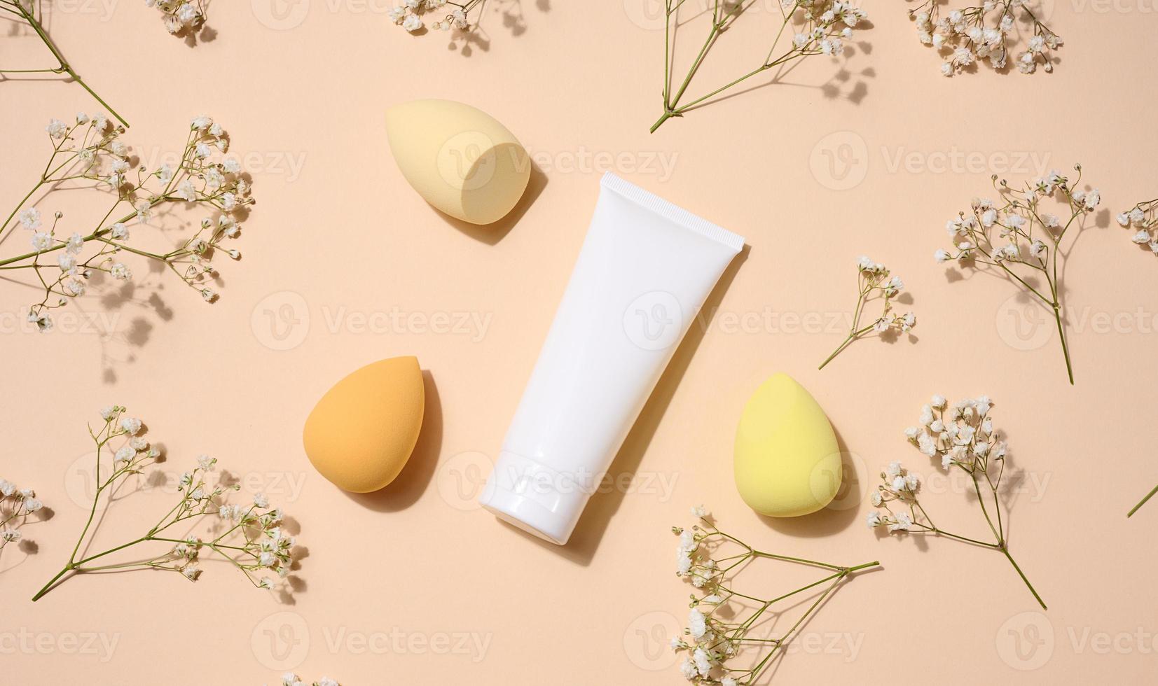 White plastic tubes for cream, gel and other cosmetics and sponges on beige background, top view photo