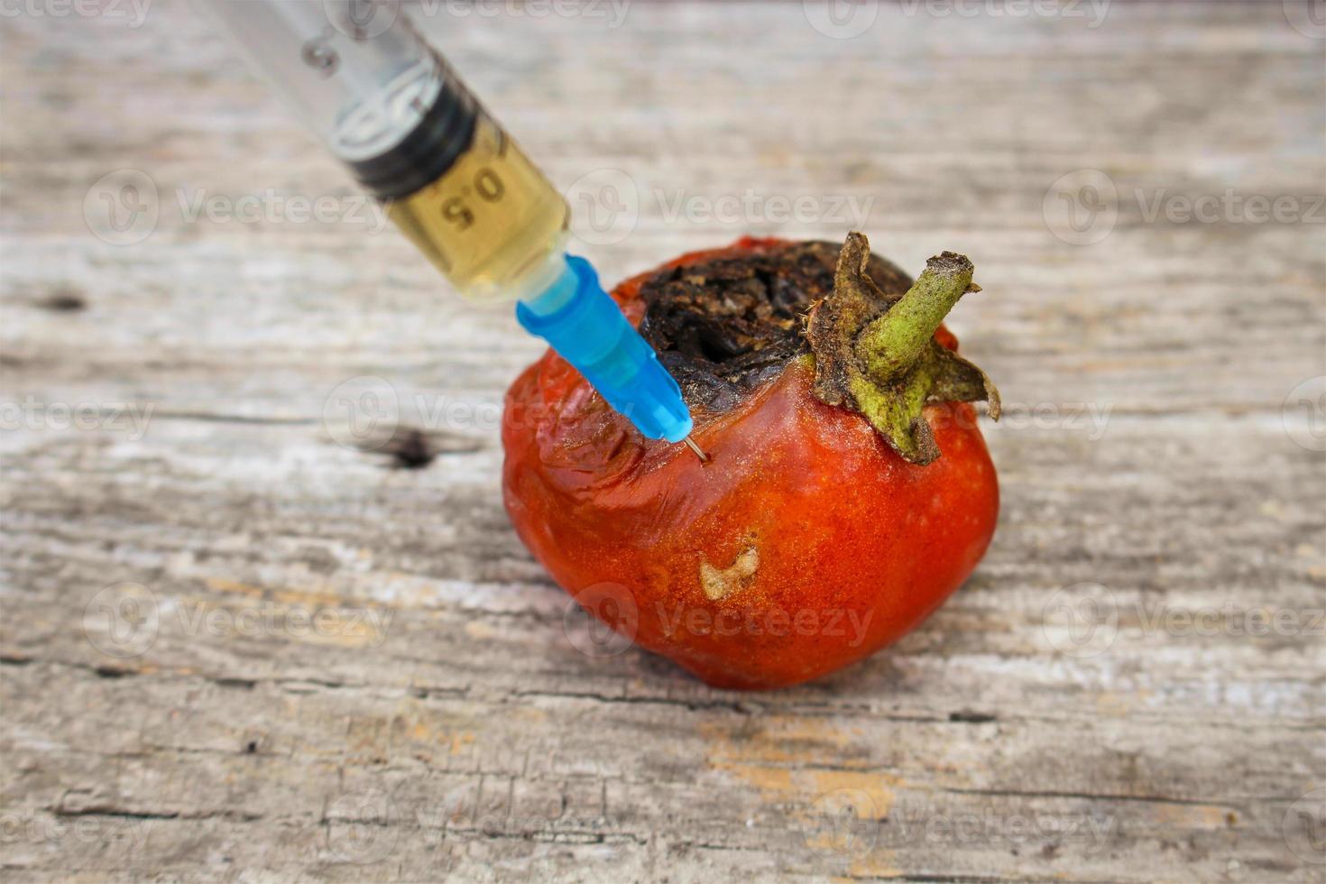 Injection of syringe in red missing tomato on wooden background. photo