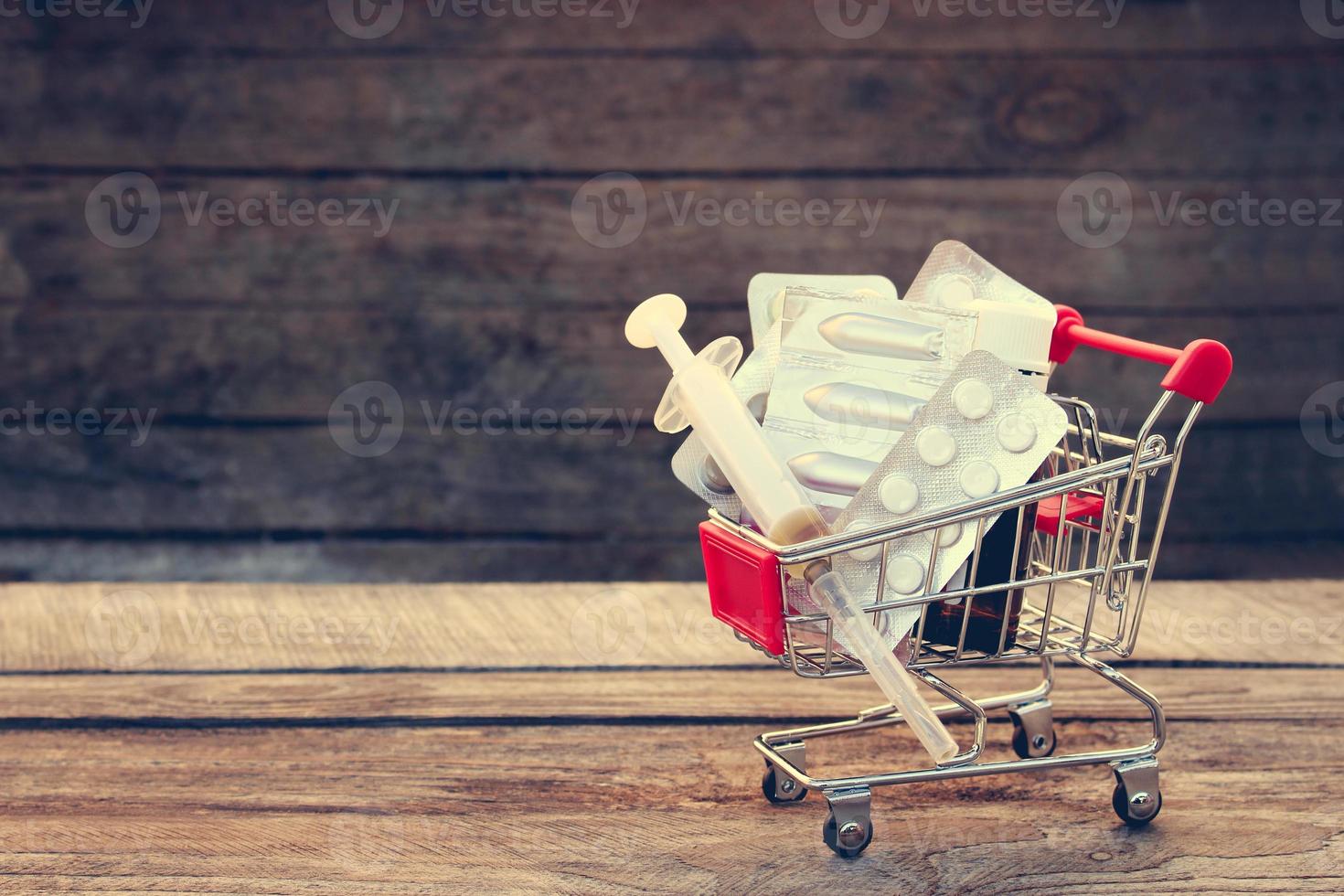 Shopping cart with pills, syringe on the old wood background. Toned image. photo