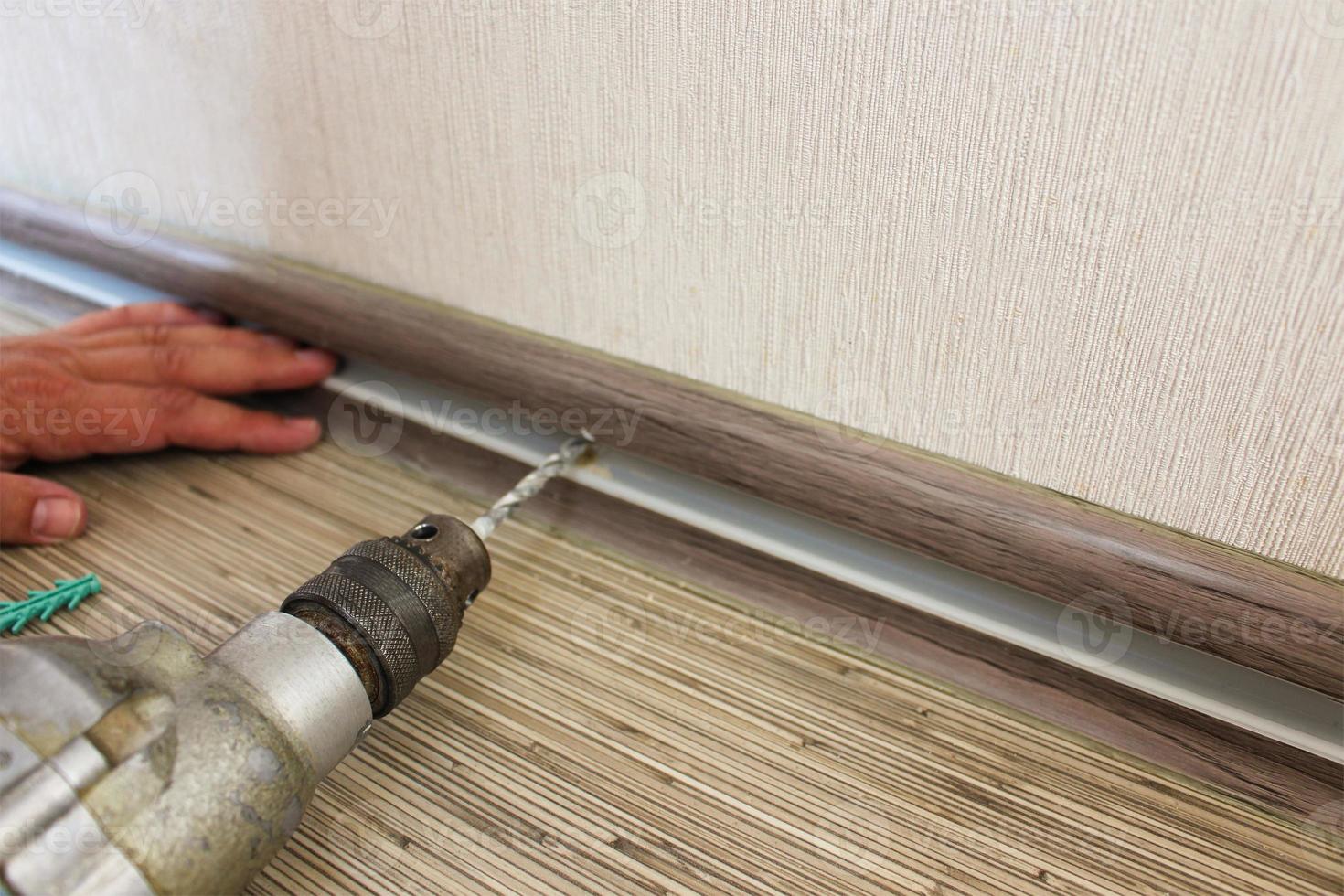 The man secures the baseboard to the wall photo