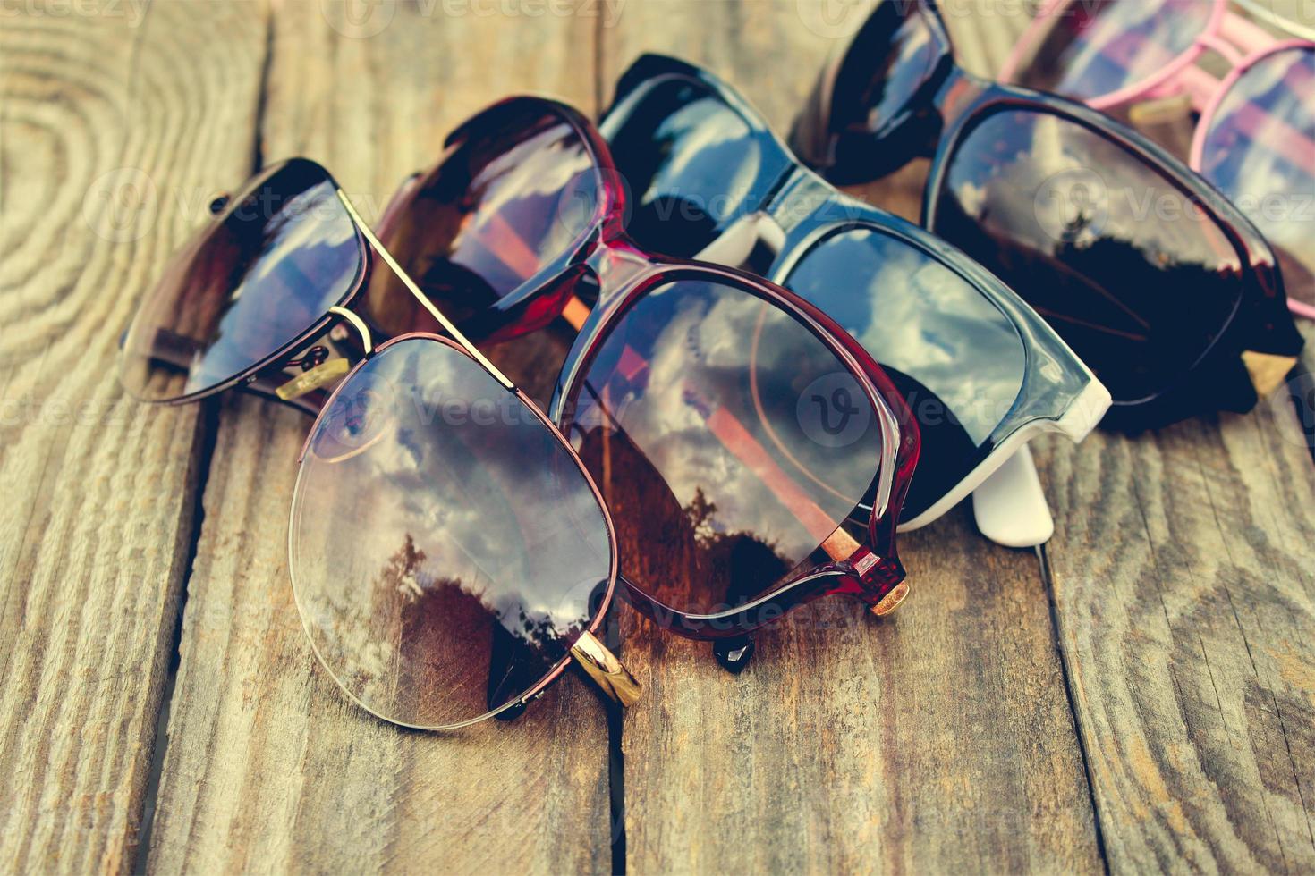 Different sunglasses on wooden background. Reflection of clouds and trees in sunglasses. Toned image. photo