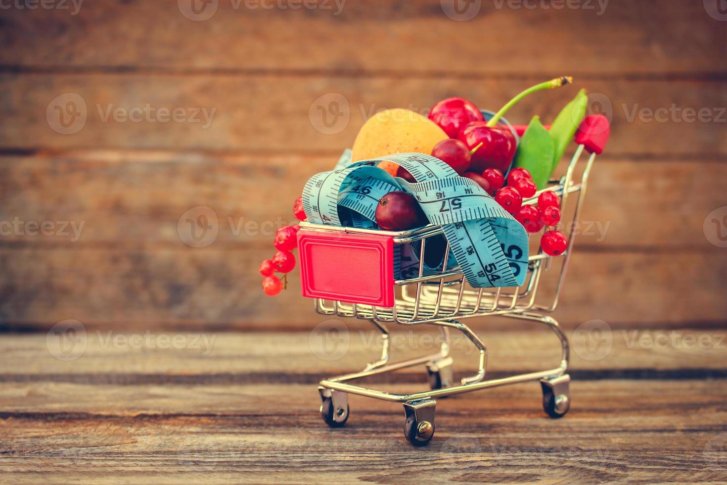 Shopping cart with fruits, berries and tape line on old wood background. Toned image. photo