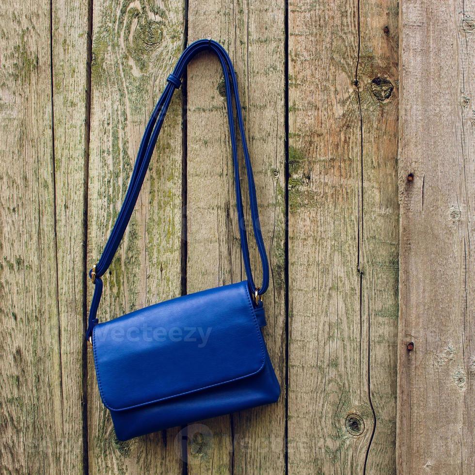 Blue women's handbag hanging on nail on old wooden background photo